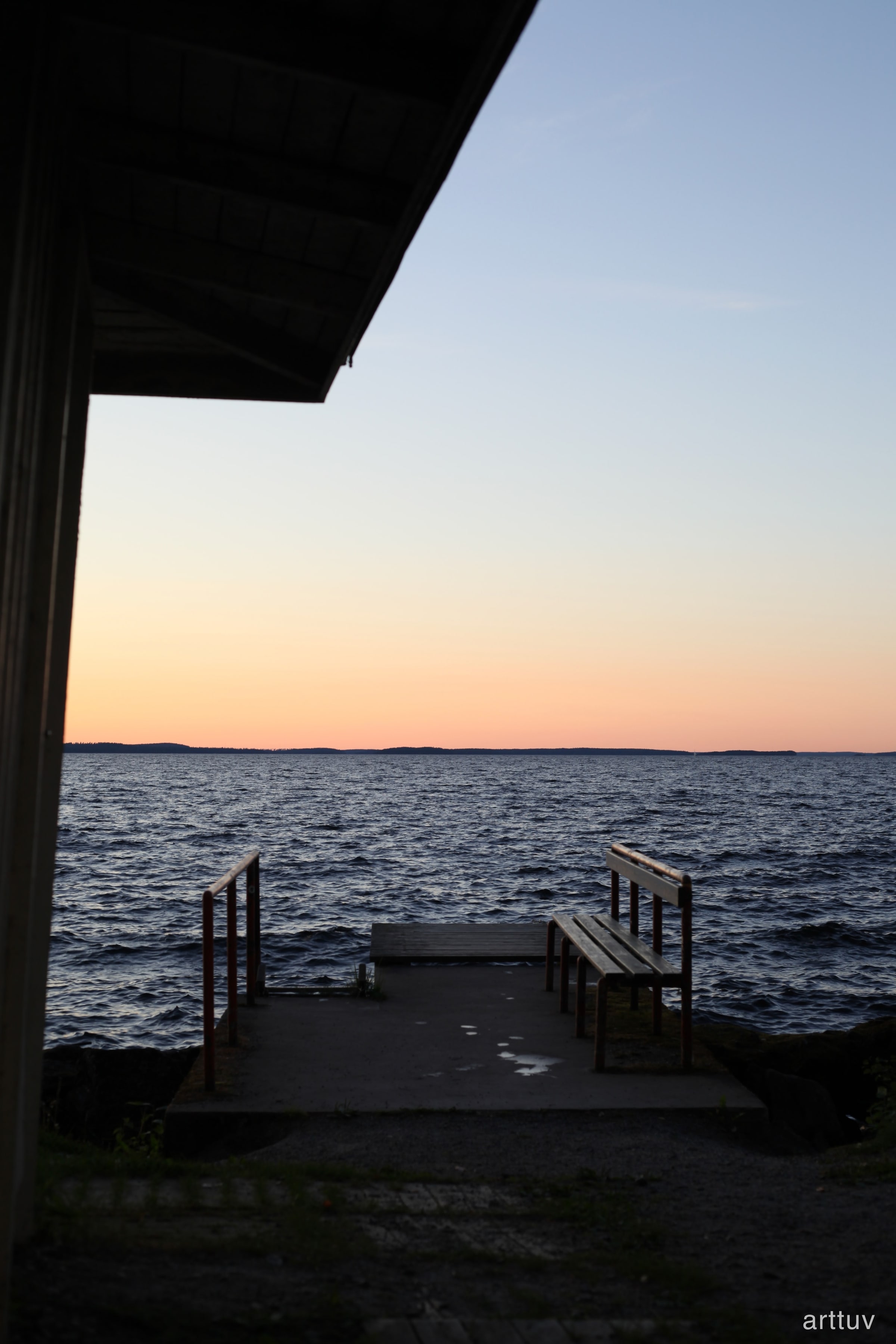 A lakeside view at dusk with dark water, a small dock, and a soft orange horizon.