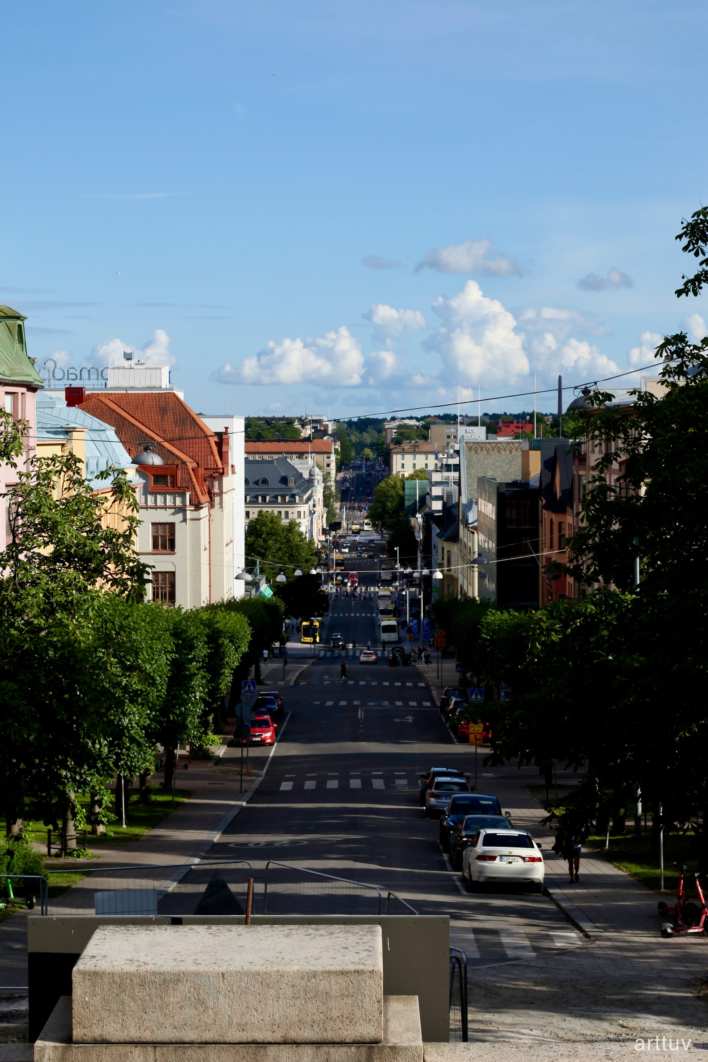 A city street descending between colorful rooftops and buildings under a bright blue sky.