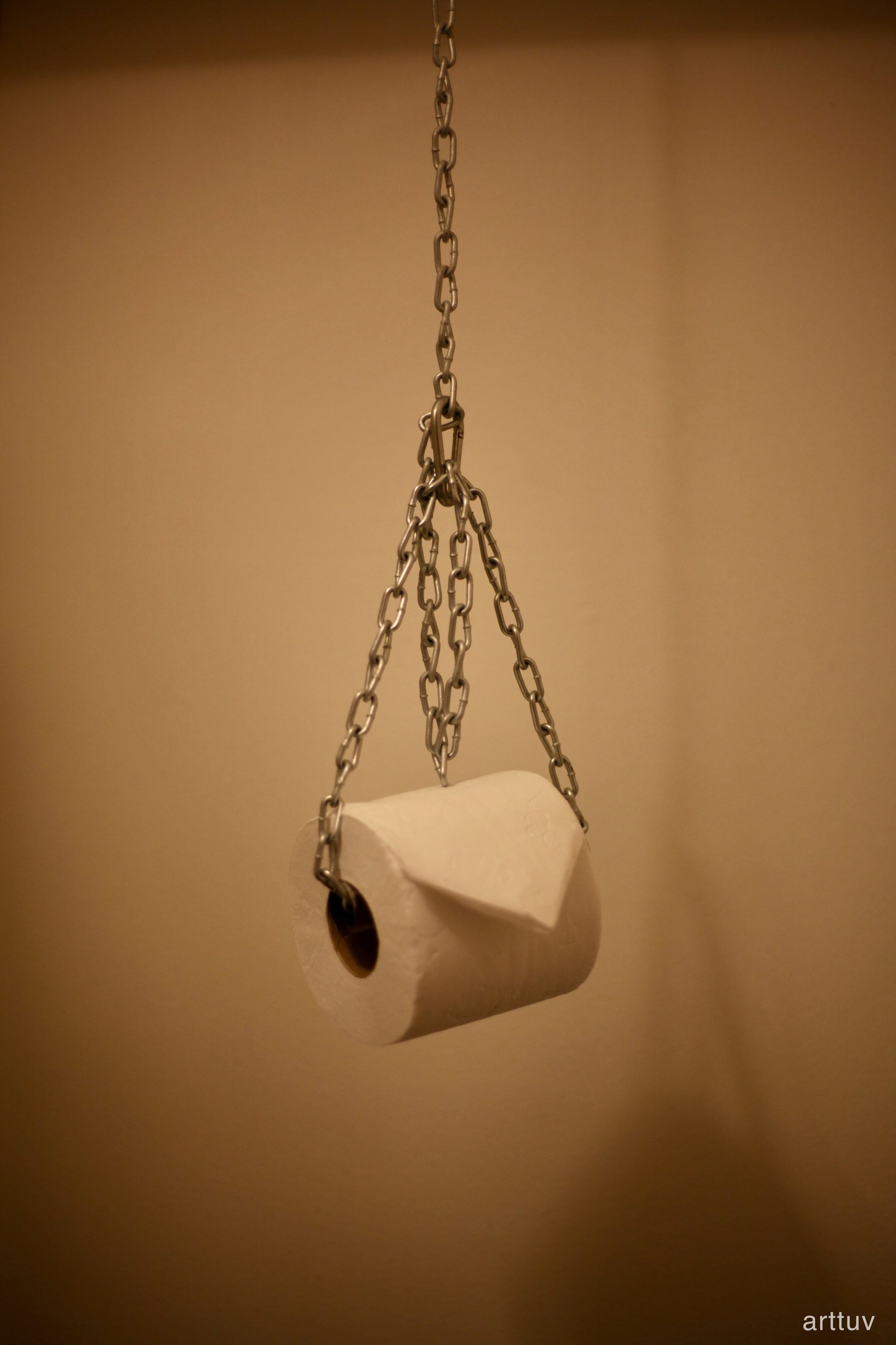 A hanging chain in soft focus against a warm wall, with part of a white seat below.