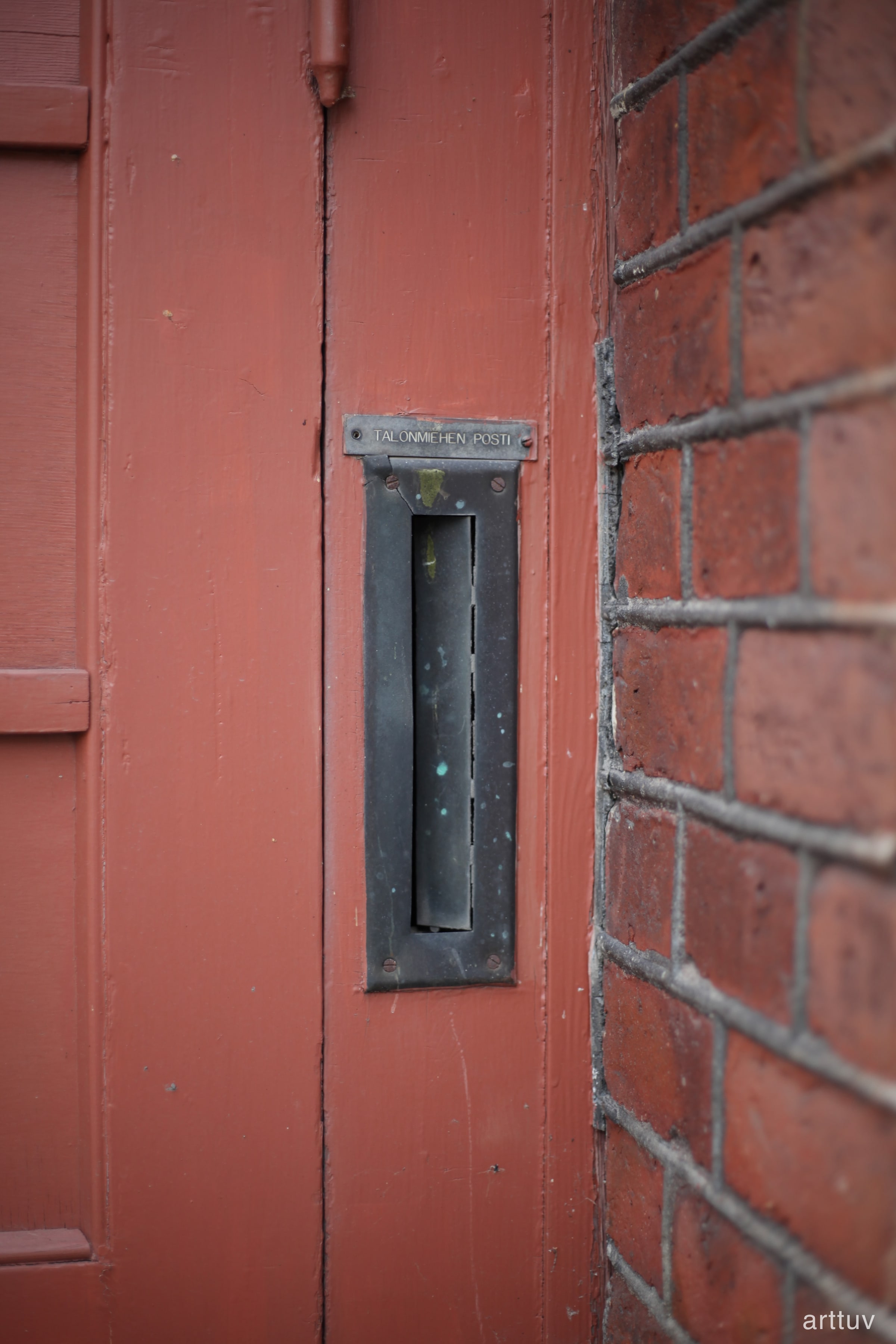 A red wooden doorway with a black metal mail slot and brickwork along the side.